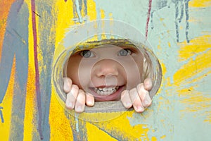 Little girl look out of the hole in painted wall.