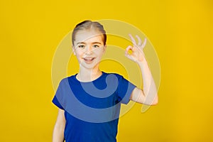 Little girl looking at camera and showing OK gesture in sign language on yellow background.