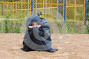 Little girl looking through a hole sitting in a black trash bag on the street, abandoned children