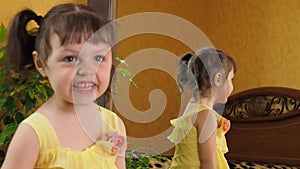 A little girl is looking in the mirror. A beautiful girl with tails on her head leans in front of the mirror. A child in a yellow