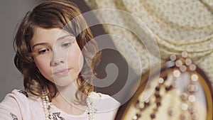 Little girl looking at mirror reflection, fitting mother's earring, childhood