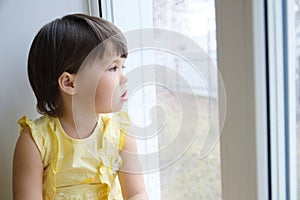 Little girl looking out the window longing for some sunshine. child sitting home at rainy day