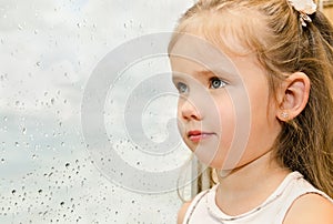 Little girl looking out the window on a rainy day