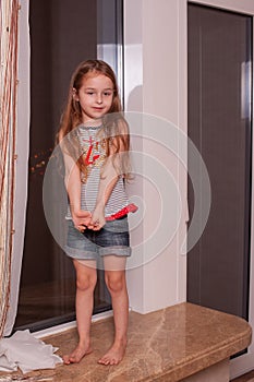 Little girl looking out window while standing on windowsill