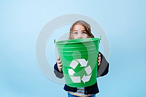 Little girl looking over green recicle bin. Holding in hands. photo
