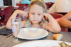 Little girl looking with sad expression face at a plate with fish cooked