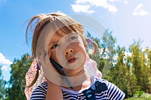 Little girl looking up and speaking by cell phone,