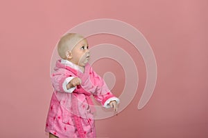 Little girl looks away in a pink bathrobe on a pink background in the studio