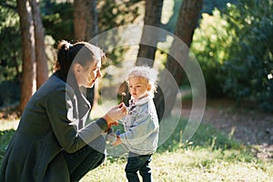 Little girl looks at a flower in her mom hand, crouching next to her in the forest