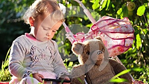 Little girl looks at her phone, she is sitting on a blanket in the garden.