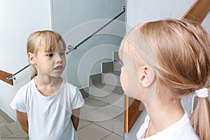 A little girl looks at herself in the mirror in the clinic. A baby tooth was pulled out.