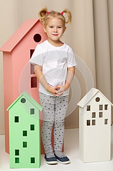 A little girl looks out from behind a toy wooden house.