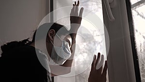 Little girl looks out the window sad in a medical gauze mask. concept pandemic virus covid lifestyle 19 self-isolation