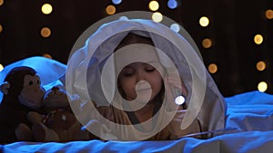 Little girl looks at pictures in a book, she holds a flashlight in her hand. Bokeh background