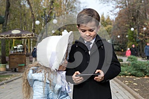 Little girl looks something interesting on screen of gadget, which her brother holding in his hands. Happy kids looking