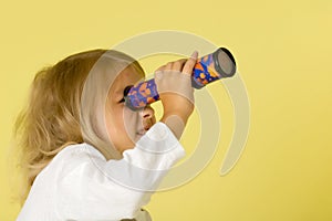 A little girl looks into a telescope or in a kaleidoscope.