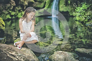 Little girl looks at the water sitting next to the bed of a rive