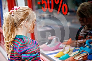 Little Girl looks at the window near the shopping center. Adorable happy child looking on shoes in store window