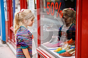 Little Girl looks at the window near the shopping center. Adorable happy child looking on shoes in store window.