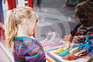 Little Girl looks at the window near the shopping center. Adorable happy child looking on shoes in store window.