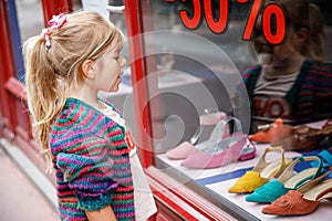 Little Girl looks at the window near the shopping center. Adorable happy child looking on shoes in store window.