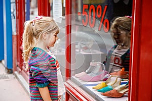 Little Girl looks at the window near the shopping center. Adorable happy child looking on shoes in store window.