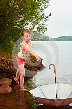 Little girl lost her umbrella in cloudy day in the lake