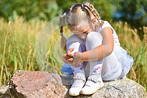 A little girl is lost in the street, sits on a rock and cries on a sunny day
