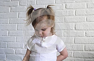 The little girl lowers her head down, looks at the floor and feels guilty or ashamed. Timid, shy kid portrait on a white