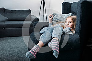 Little girl lying in armchair with pillow and looking at camera