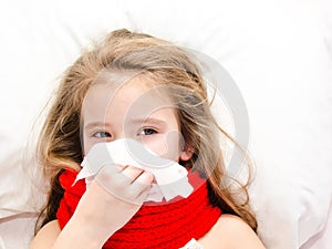 Little girl lying in the bed and blowing her nose