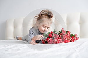 Little girl lying on bed with bouquet of pink roses