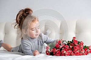 Little girl lying on bed with bouquet of pink roses