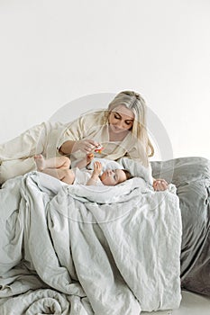 A little girl is lying in bed with cookies in her hands. The mother is lying next to her daughter, holding a pacifier in her hands