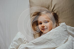 Little girl lying in bed covered in blanket at home
