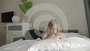 Little girl is lying on the bed and looking into her smartphone.