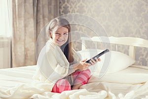 Little girl lying in bed with a remote control TV