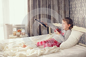 Little girl lying in bed with a remote control TV