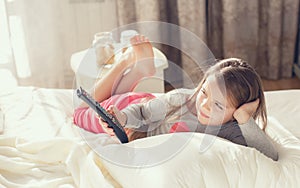 Little girl lying in bed with a remote control TV