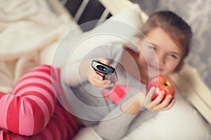 Little girl lying in bed with a remote control TV