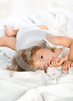 Little girl lying in bed and sucks a finger