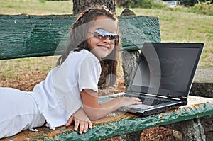 Little girl lying on a bench with your computer