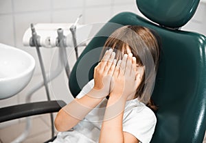 little girl lying in a dentist chair and covering her eyes, being afraid of the checkup at the dentists