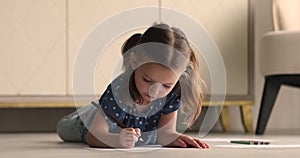 Little girl lying on floor draws with pencils in album