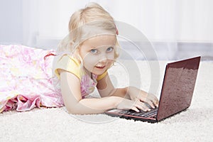 Little girl lying on floor working with a laptop