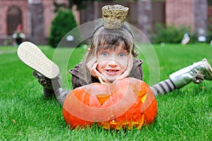 Little girl lying on a grass with big pumpkin