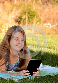 A little girl lying on the grass with her tablet.