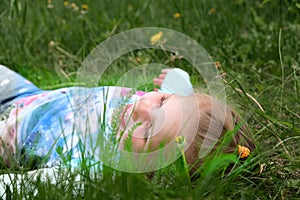 Little girl lying on grass lawn smiling. Summer fun outdoors. Happy child enjoying on grass field and dreaming