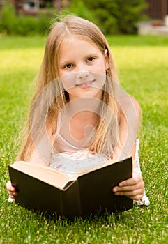 Little girl lying on grass and read book