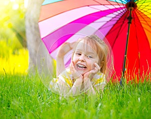 Little girl lying on green grass under the colorful umbrella